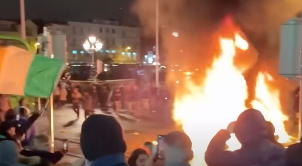 Polisbilar slogs sönder, vältes och brändes i upploppen. Utåt sett påminner scenerna om de invandrarupplopp som skakat Sverige flera gånger – men det är istället, åtminstone till stor del, vita irländska ungdomar som är arga över invandringen. Skärmavbild: Newsweek